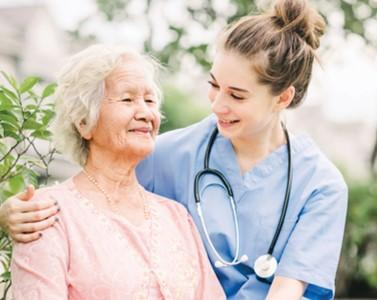 Smiling nurse with her arms around a smiling elderly lady
